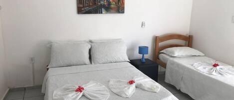 A hotel room with a large bed, two smaller beds, and a painting on the wall.