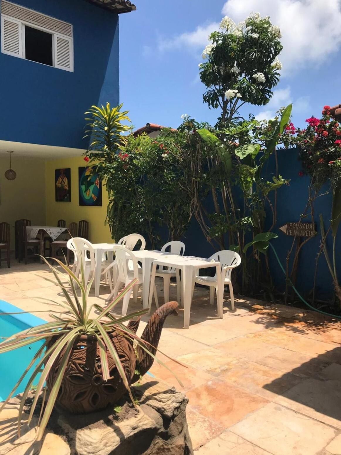 A blue building with a patio area featuring a pool, white plastic chairs, and potted plants.