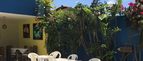 A blue building with a patio area featuring a pool, white plastic chairs, and potted plants.