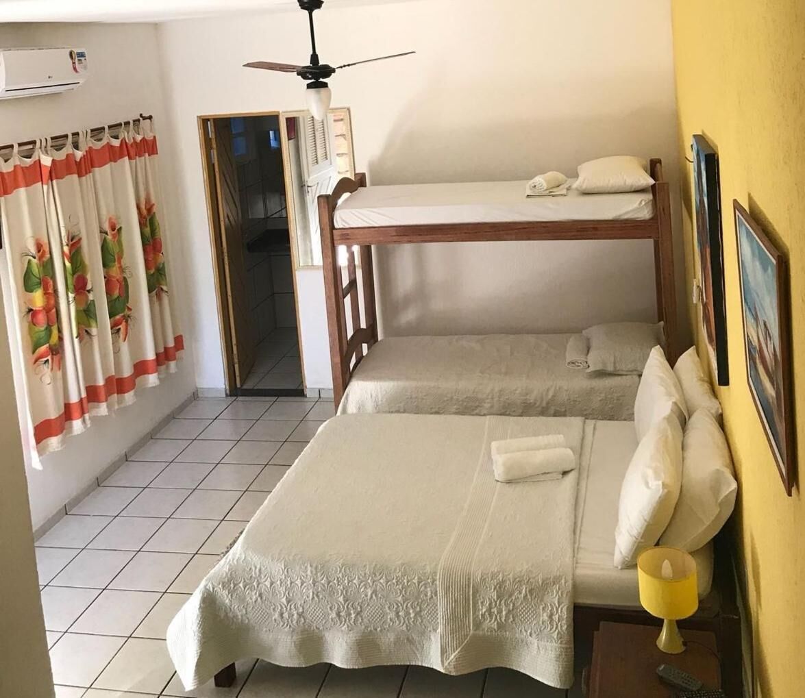 Ein Zimmer mit zwei Betten, einem Deckenventilator, einem Fenster mit Vorhängen und einer Wand-Klimaanlage.