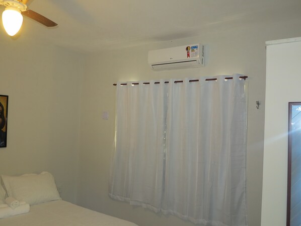 A hotel room with a bed, a ceiling fan, an air conditioning unit, and a window with a sheer curtain. - Pousada Pé na Areia (Tibau do Sul)
