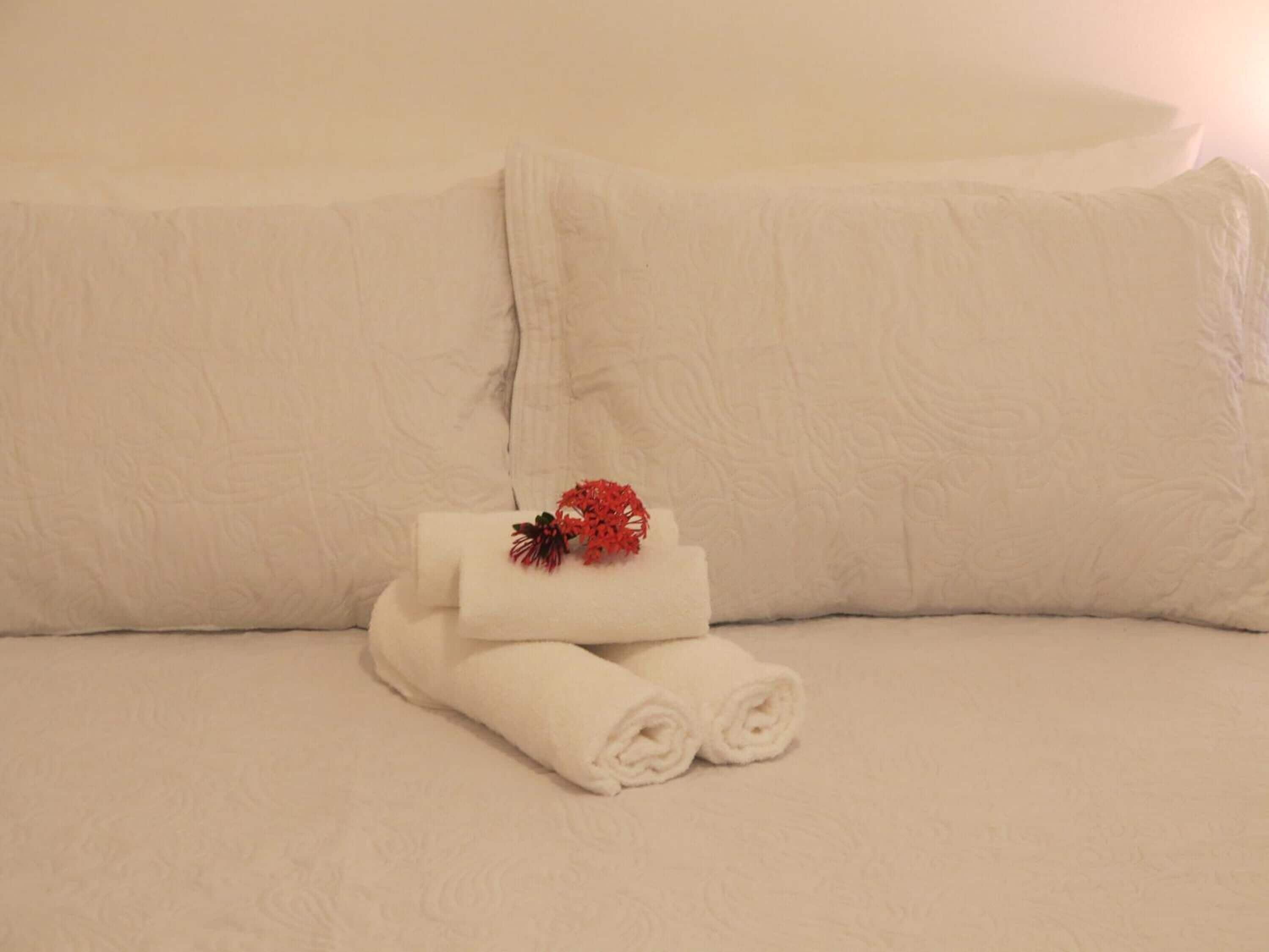A neatly made bed with white linens and a decorative red floral arrangement on top.