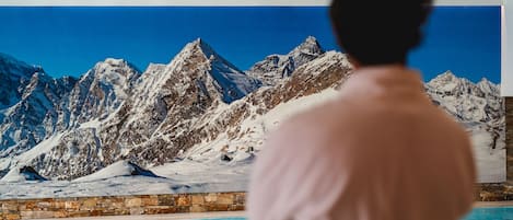A person standing by a pool with a mural of snow-covered mountains in the background.