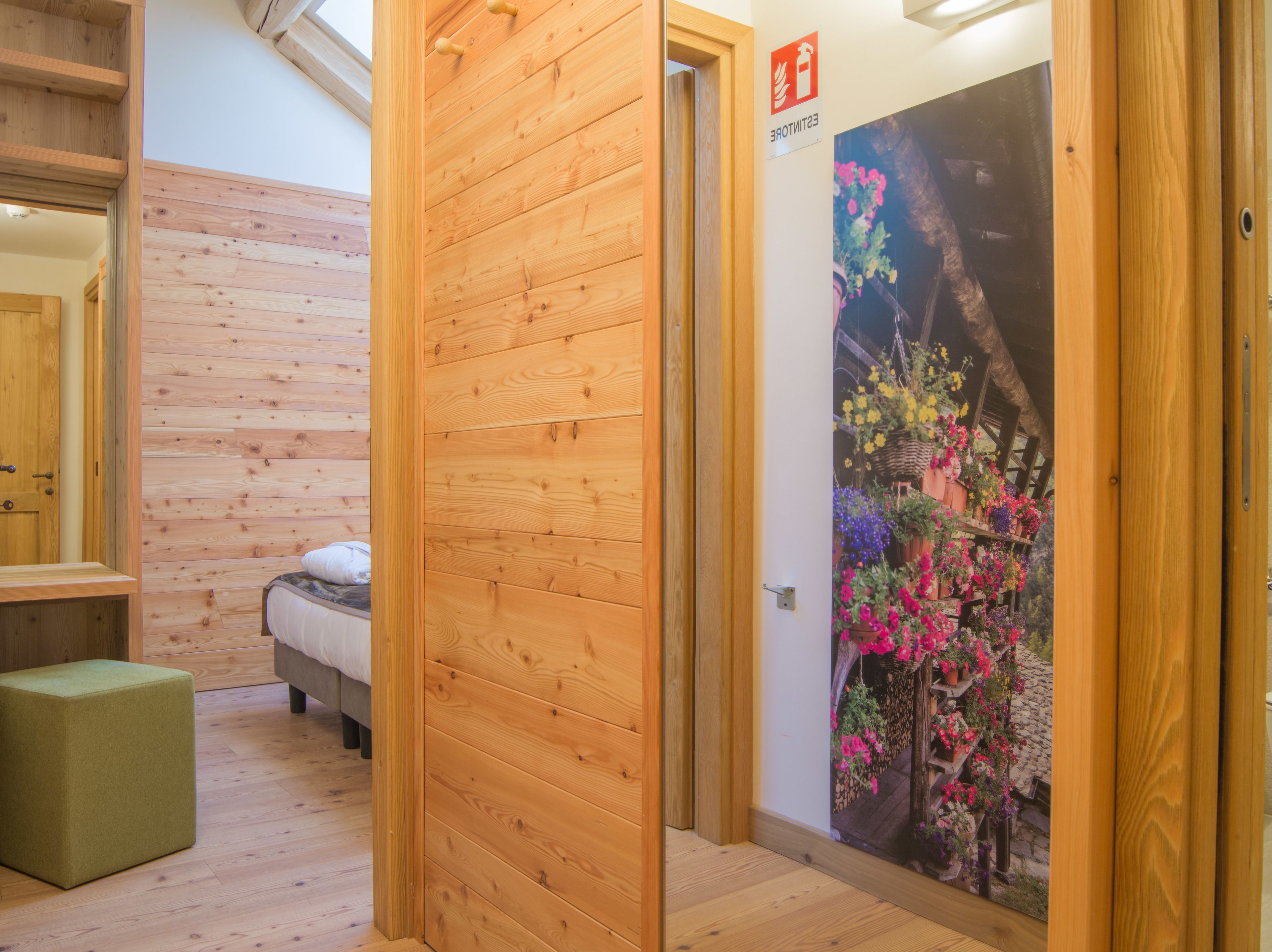 Een houten kamer met een bed, een groene poef en een muur met een bloemenposter.