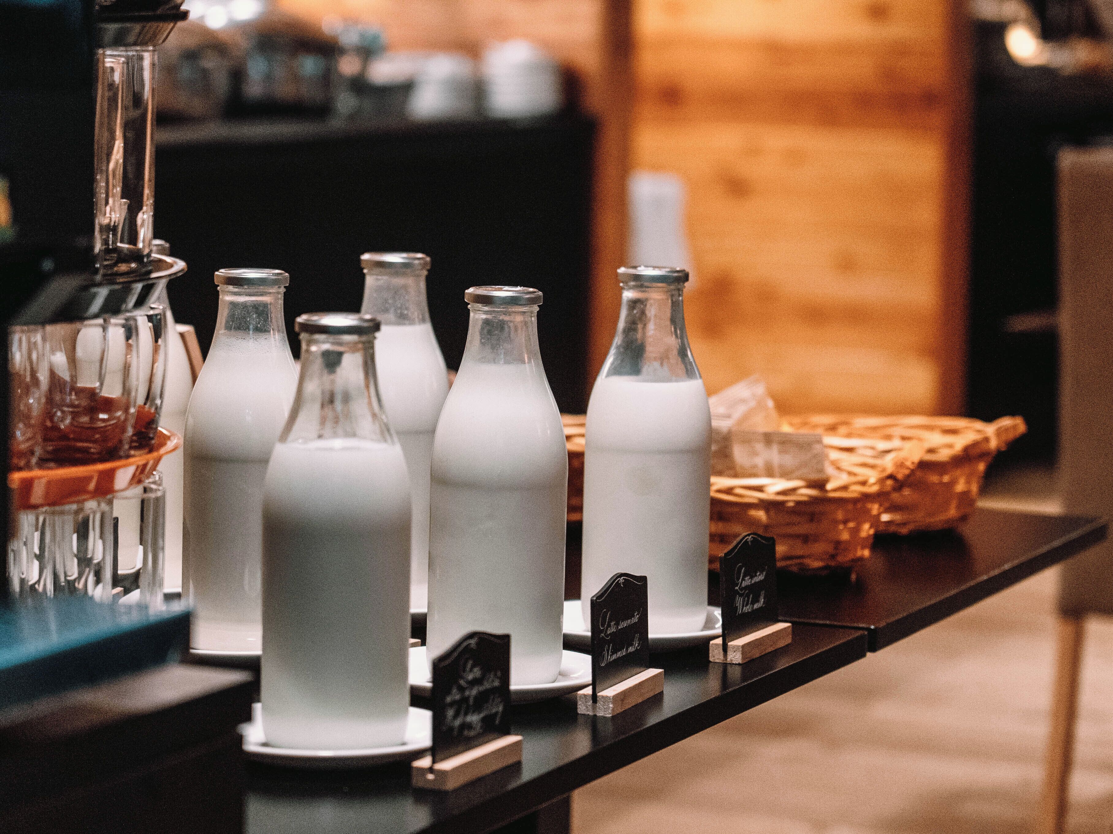 A selection of milk bottles on a counter with labels, a blender, and a basket in the background.