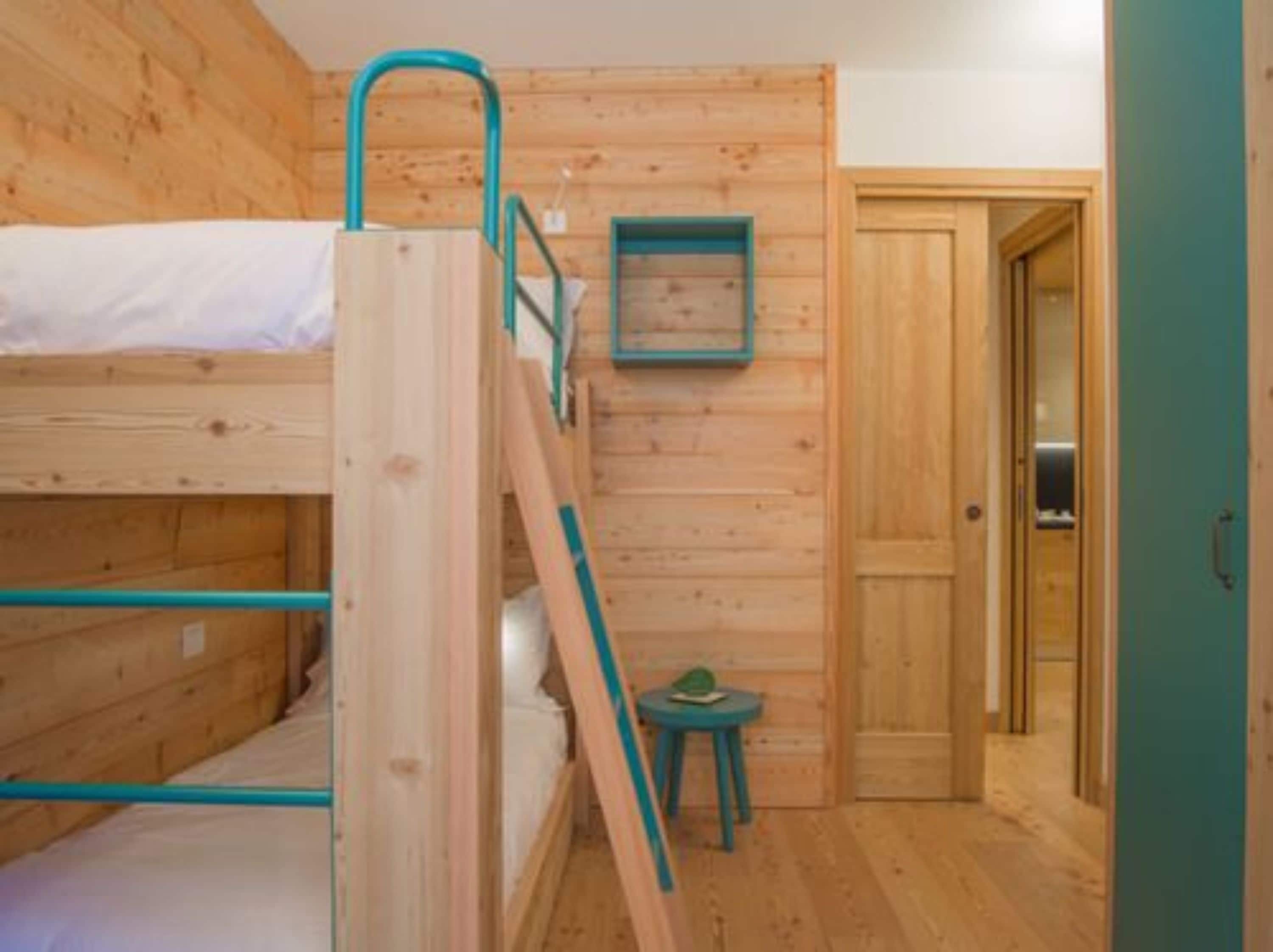 A bunk bed room with wooden walls, a small table, and a door.