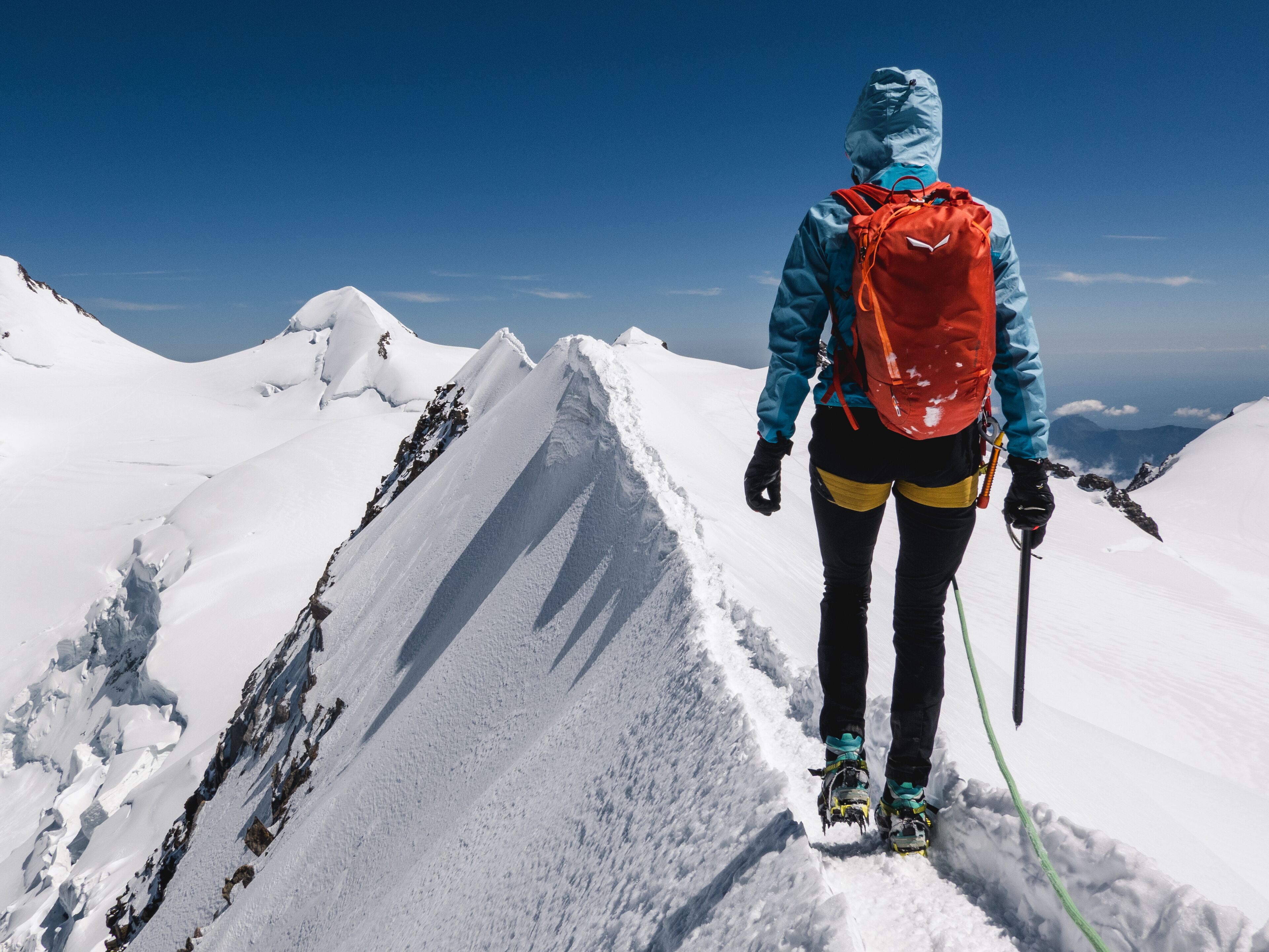 Une personne se tient sur une crête montagneuse enneigée, sous un ciel dégagé.