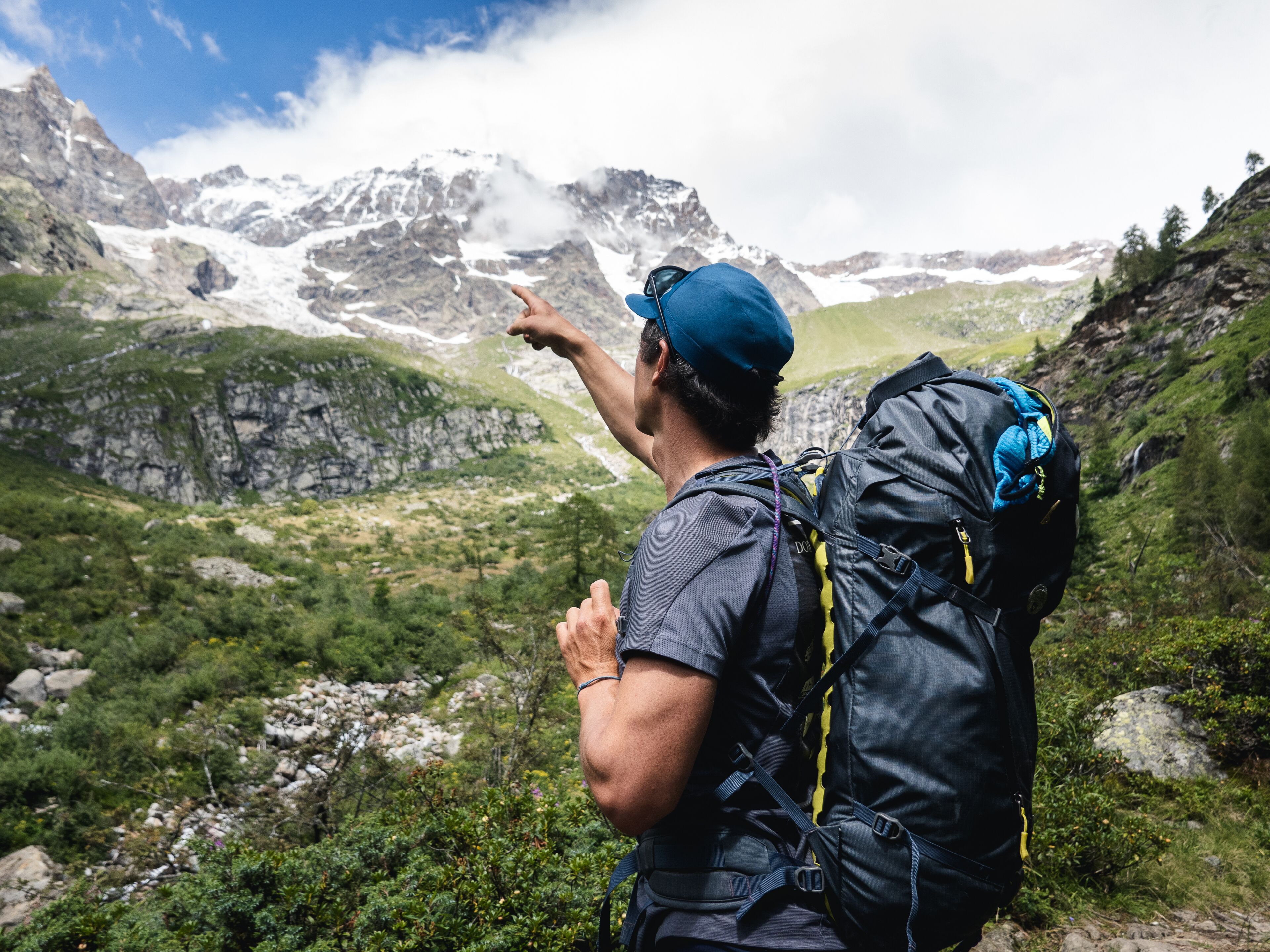 A person hiking with a backpack, pointing towards a mountainous landscape.