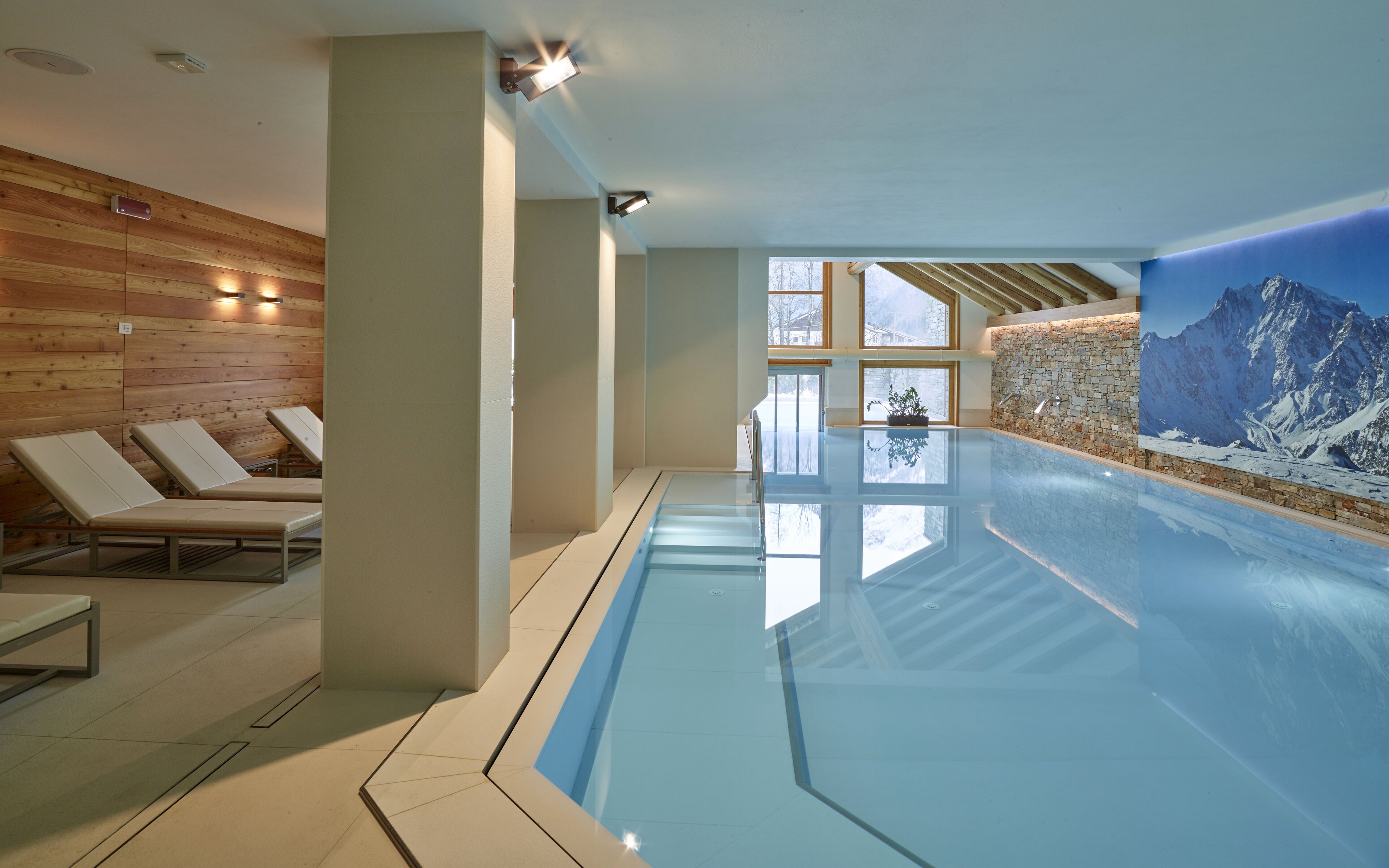 Una piscina interna con pareti in legno, poltrone relax e vista sulle montagne.