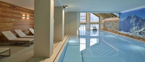 An indoor swimming pool with wooden walls, lounge chairs, and a mountain view.