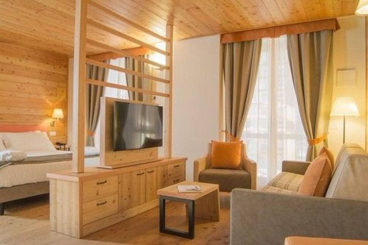 Une pièce chaleureuse avec un plafond en bois, un lit, un téléviseur posé sur un meuble en bois, un canapé et une fenêtre avec des rideaux.