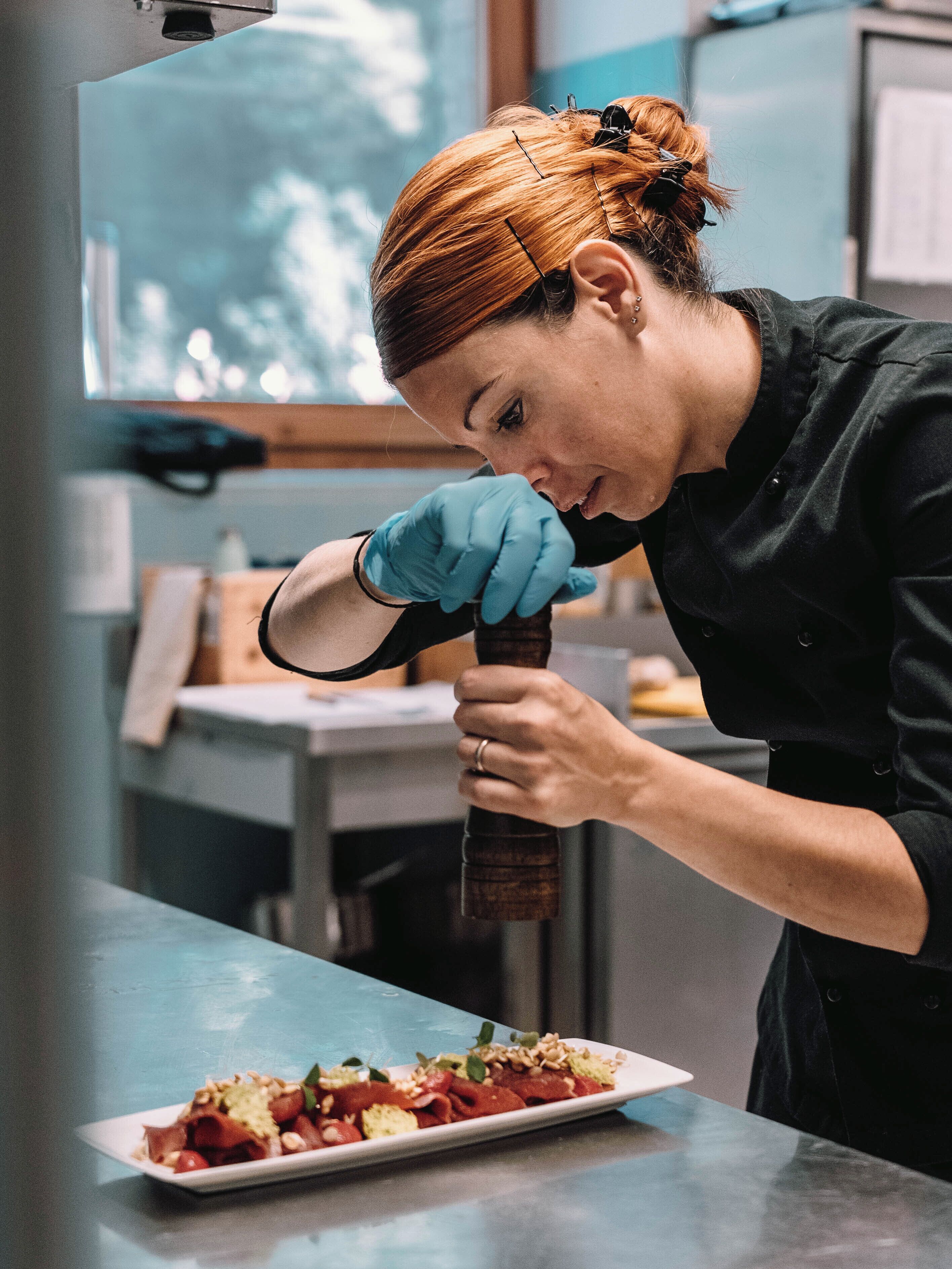 A person in a black uniform with blue gloves preparing food on a counter.
