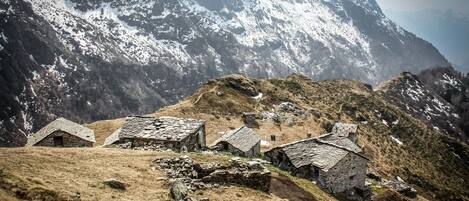 A mountainous area with stone buildings, some with thatched roofs, and snow-capped peaks in the background.
