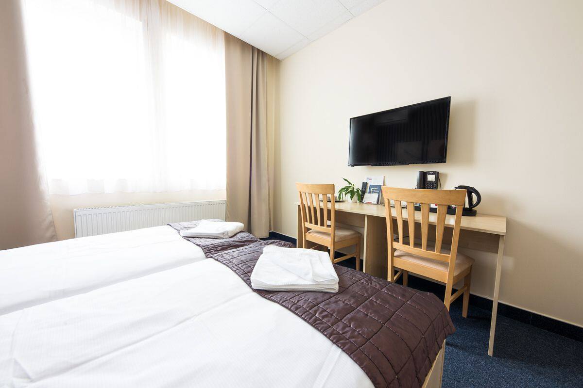A hotel room with two beds, a desk with a chair, a television, and a coffee maker.