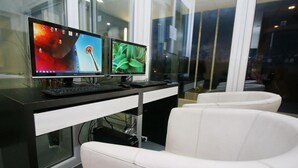 Un espacio de oficina moderno con dos monitores en un escritorio, una silla de cuero blanco y vistas amplias a través de grandes ventanales.