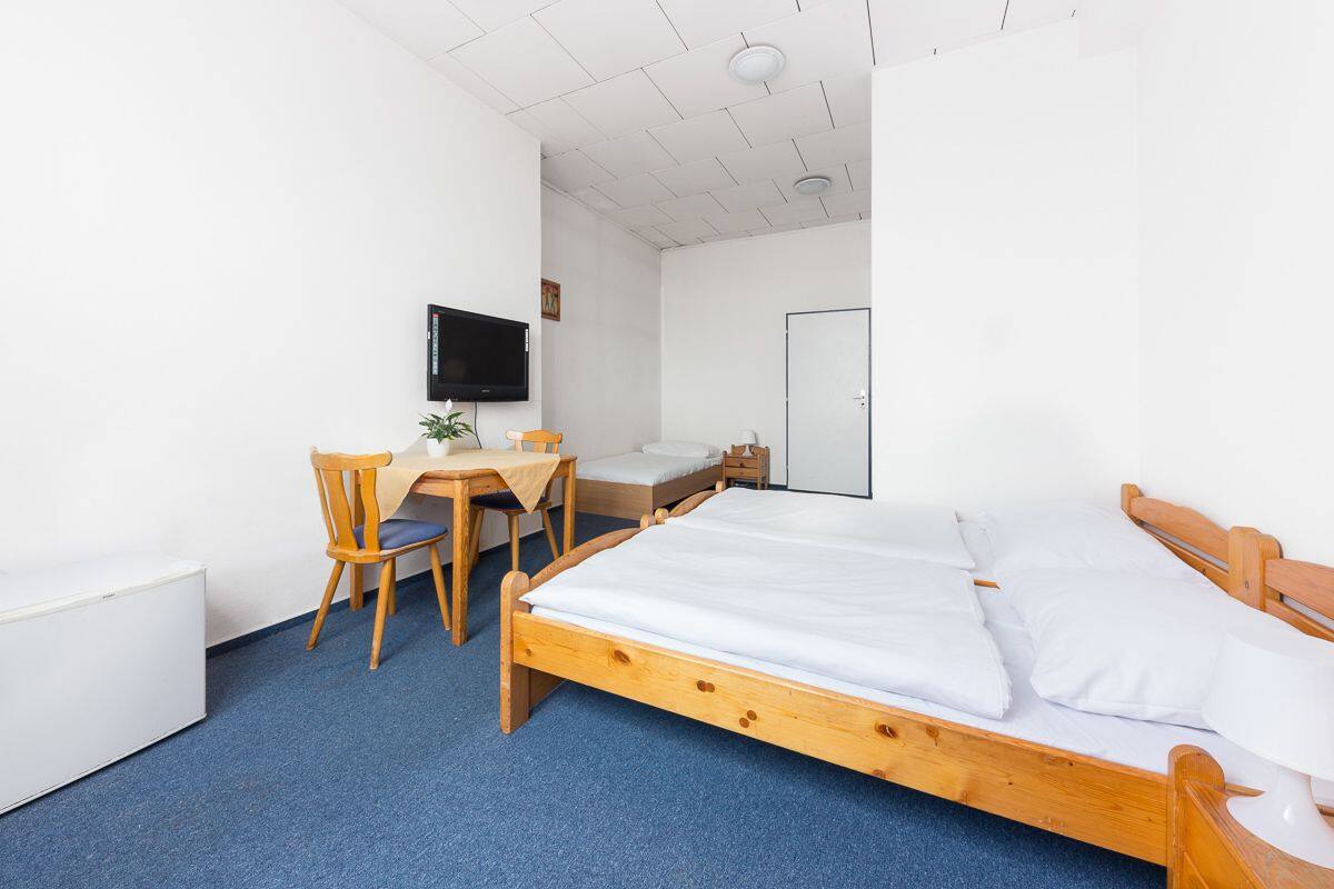 A bedroom with a wooden bed, a desk with a chair, a television, and a white door.