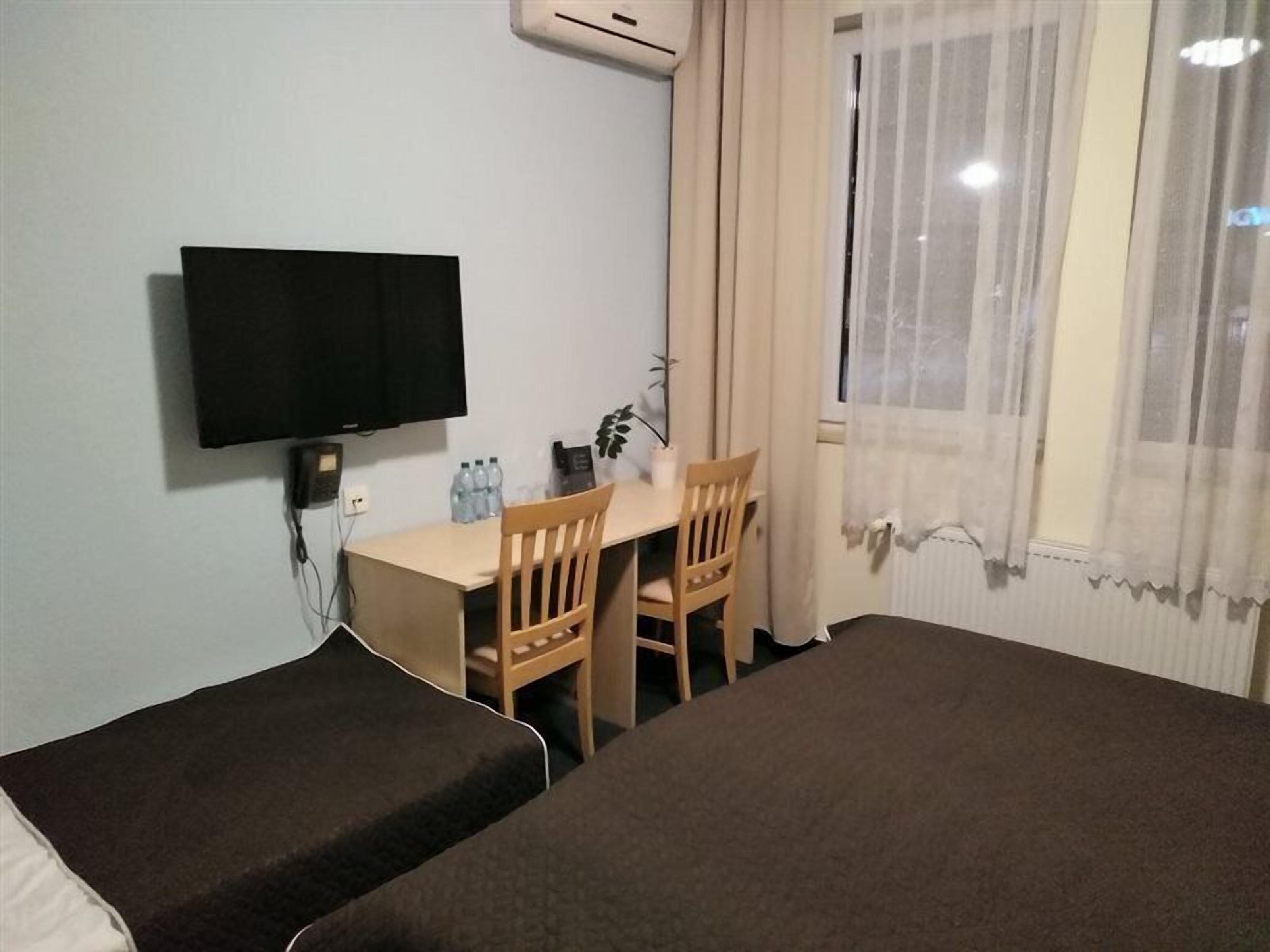 Une chambre d’hôtel comprenant un lit, un bureau, deux chaises, une télévision et une fenêtre avec des rideaux.