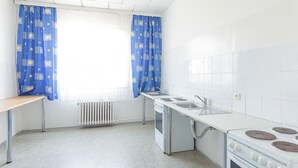 Una cocina pequeña con azulejos blancos, estufa, pileta y ventana con cortinas azules.