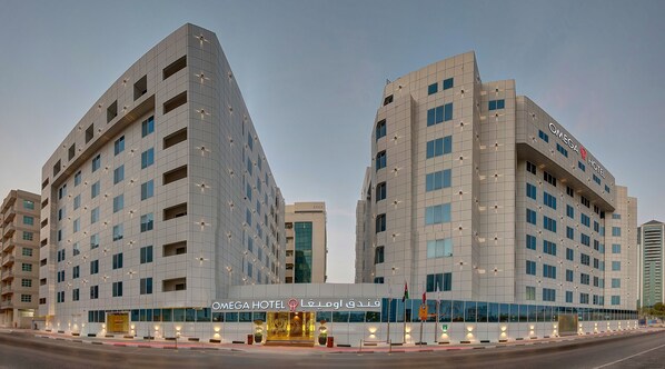 A modern hotel with a prominent Omega Hotel sign, featuring a grid-like facade with evenly spaced windows and a symmetrical design. - Omega Hotel (Dubai)