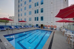A swimming pool with blue tiles, surrounded by lounge chairs and red umbrellas. - Omega Hotel (Dubai)