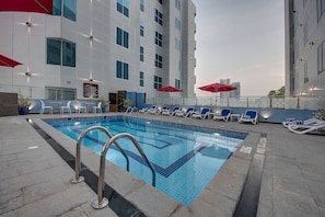 A swimming pool with lounge chairs and umbrellas, surrounded by a modern building with large windows. - Omega Hotel (Dubai)
