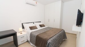 A bedroom with a bed, bedside table, lamp, TV, and wardrobe. - Morada Clariana (Curitiba)
