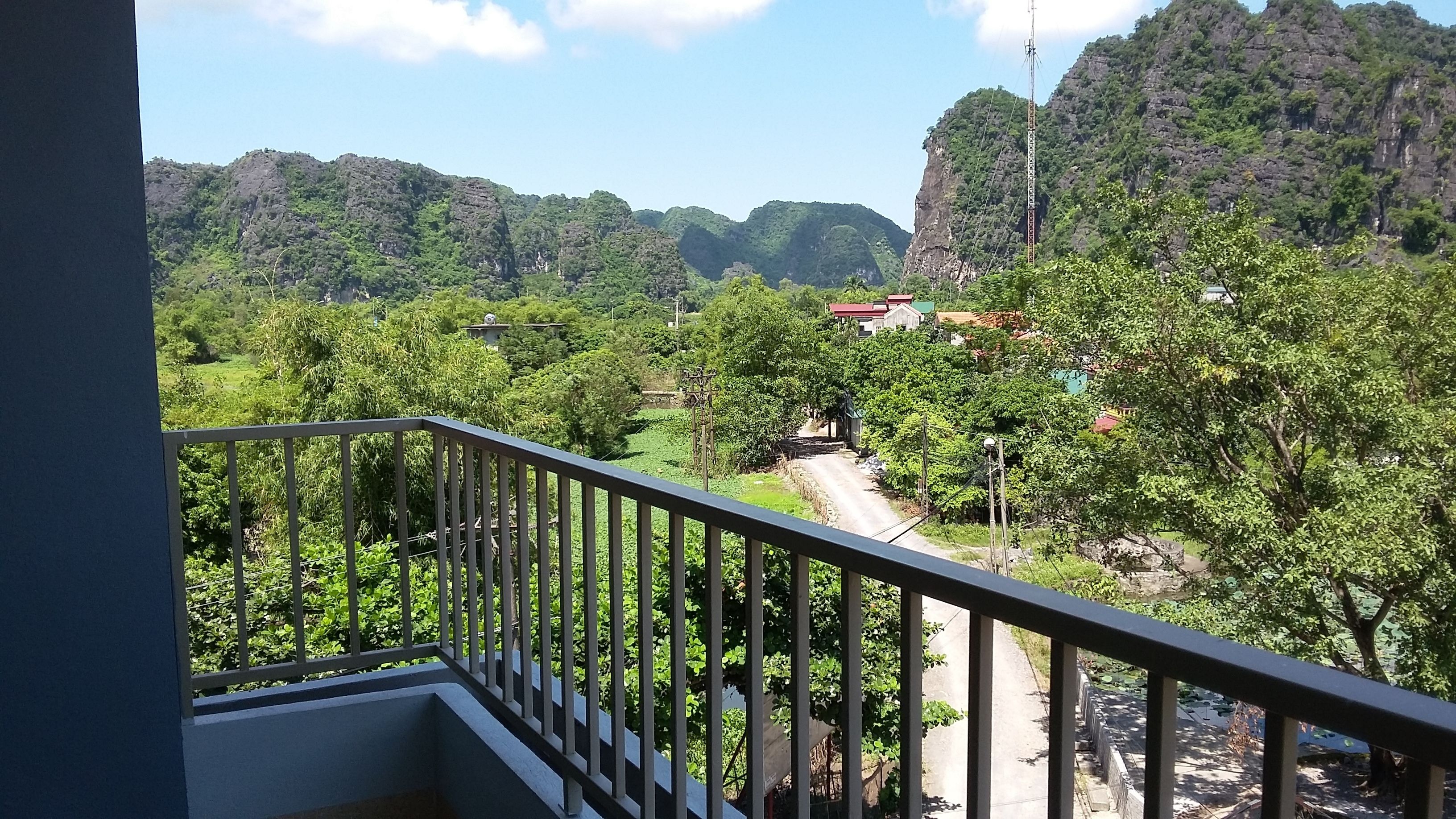 A balcony with a view of a rural landscape, including a road, trees, and a building with a red roof.