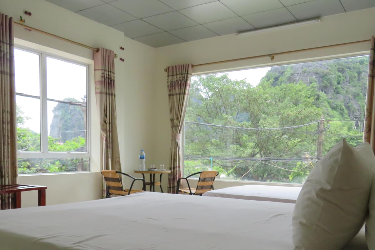 Ein Hotelzimmer mit einem großen Bett, zwei Stühlen, einem kleinen Tisch und Blick auf Grünflächen.