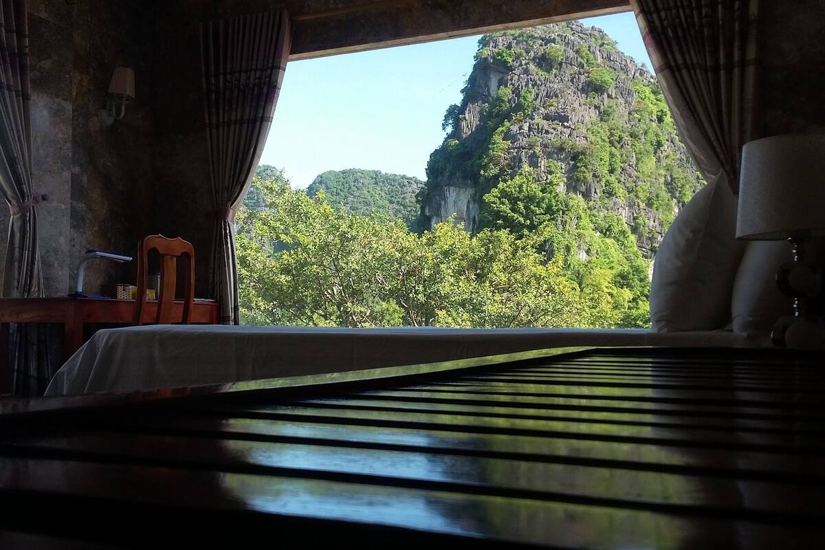 Ein Zimmer mit einem Bett, Vorhängen, einem Sessel und Blick auf eine gebirgige Landschaft.