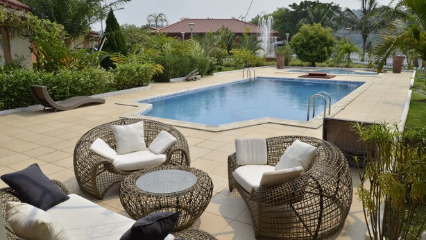 Un área de piscina con mobiliario de mimbre y una fuente.