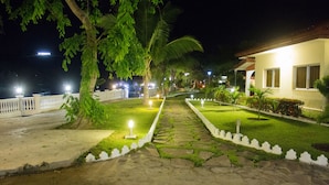 Vista nocturna de un hotel con un sendero iluminado que lleva a la entrada, rodeado de vegetación y palmeras.