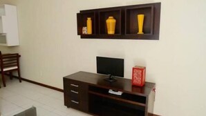 A room with a dark wooden TV stand, a flat-screen TV, and a shelf with three yellow vases.