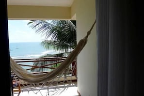 A hammock on a balcony with a view of the ocean and palm trees.