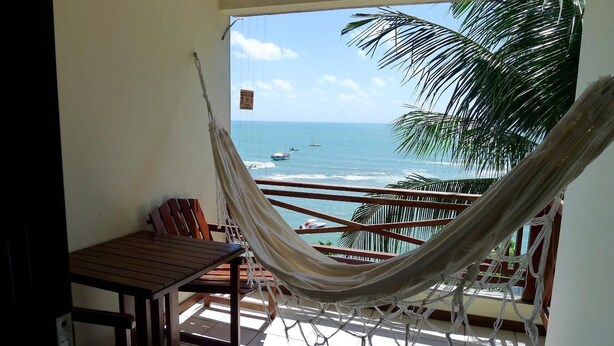 A balcony with a hammock, wooden furniture, and a view of the ocean.