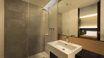 Un baño moderno con un espejo grande, ducha y lavamanos.