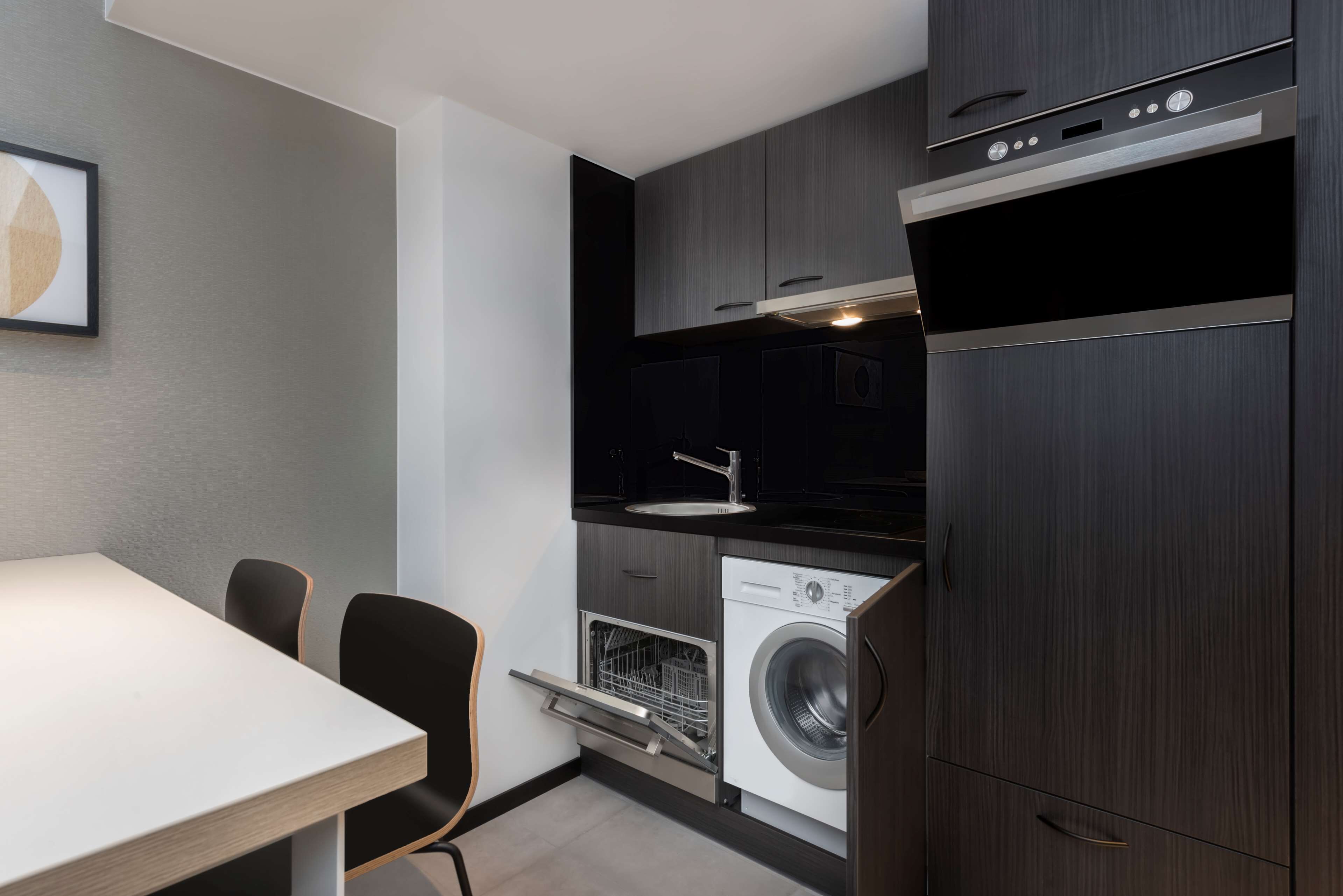 Cocina compacta con lavadora y secadora integradas, un lavamanos y una zona de comedor con sillas.