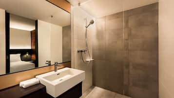 Un baño moderno con un espejo grande, un lavamanos blanco y una ducha con cabezal de ducha manual.