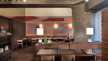 Un restaurante moderno con mobiliario de madera, un mural abstracto y colorido, y una zona de estar acogedora.