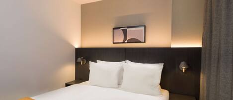 Habitació d'hotel amb llit, dues làmpades de nit, un quadre encimbellat sobre el llit i un capçal de llit fosc.