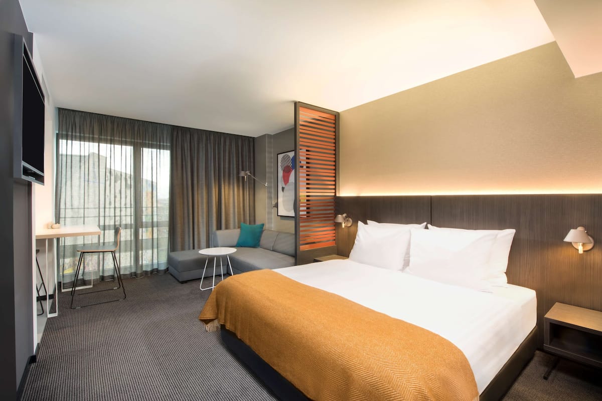 Ein Hotelzimmer mit einem großen Bett, einem Schreibtisch, einer Couch und Blick auf die Stadt.