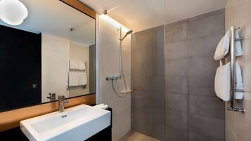 A modern bathroom with a white sink, a large mirror, and a shower area.