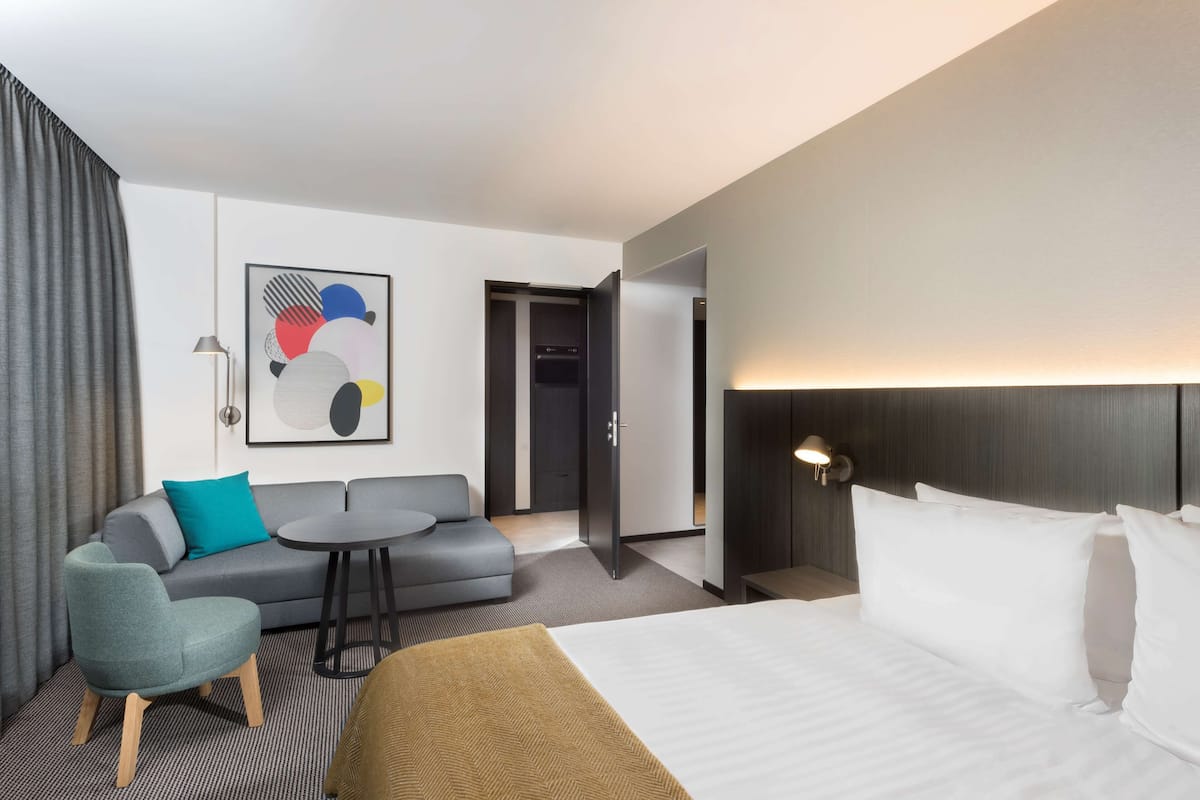 Ein modernes Hotelzimmer mit einem Bett, einer Couch, einem kleinen runden Tisch und einem Bild an der Wand.