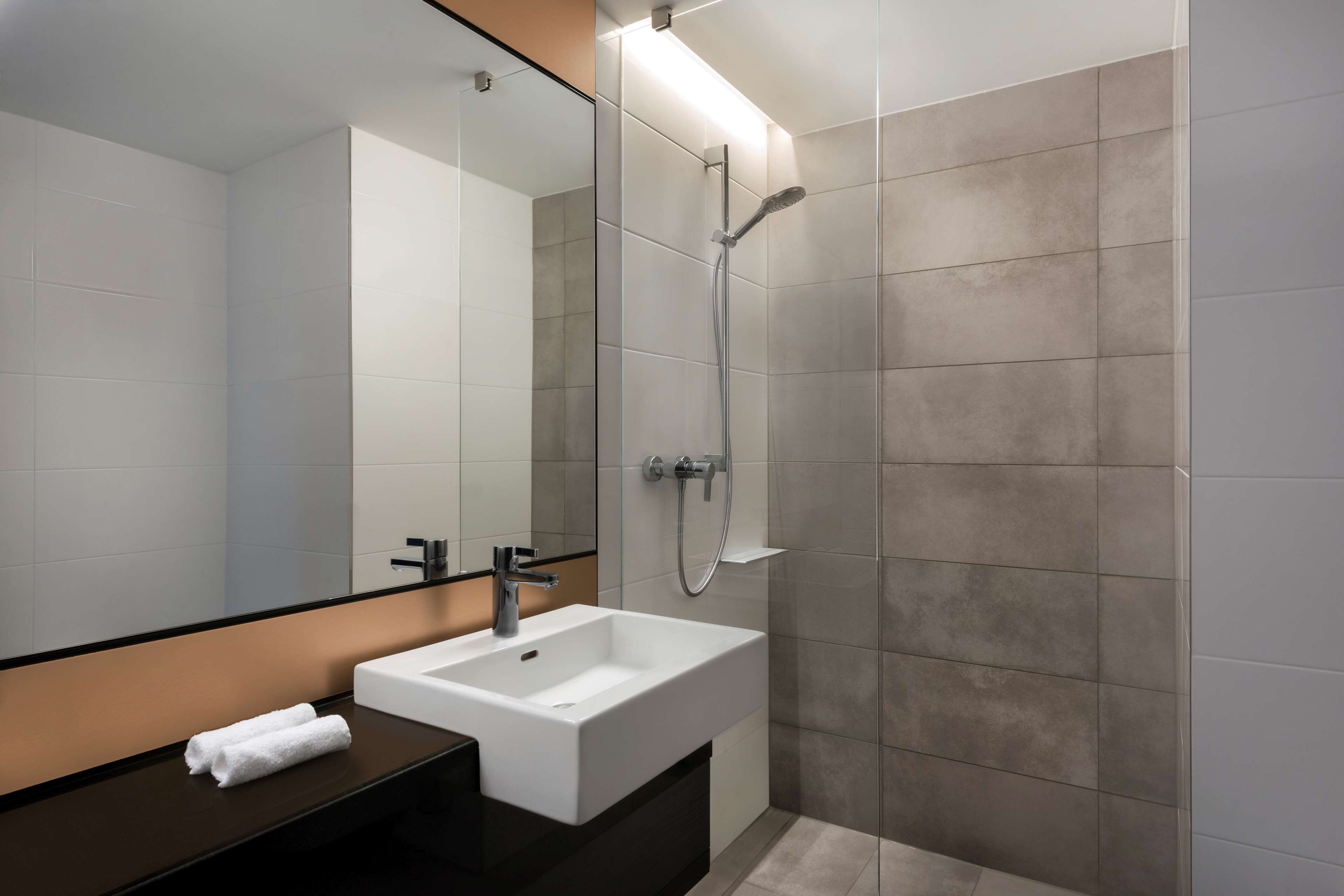Ein modernes Badezimmer mit einem weißen Waschbecken, einem Spiegel und einer Dusche.
