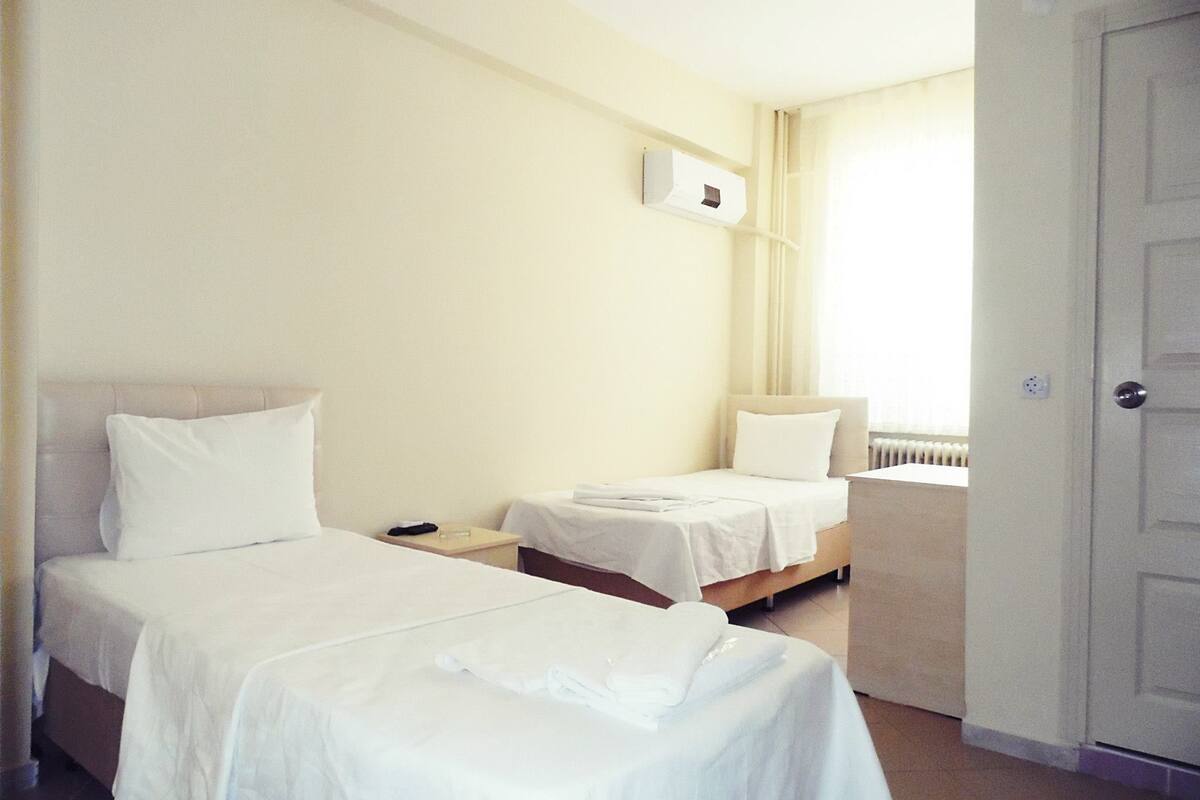 A hotel room with two single beds, a bedside table with a lamp, a radiator, and a door.