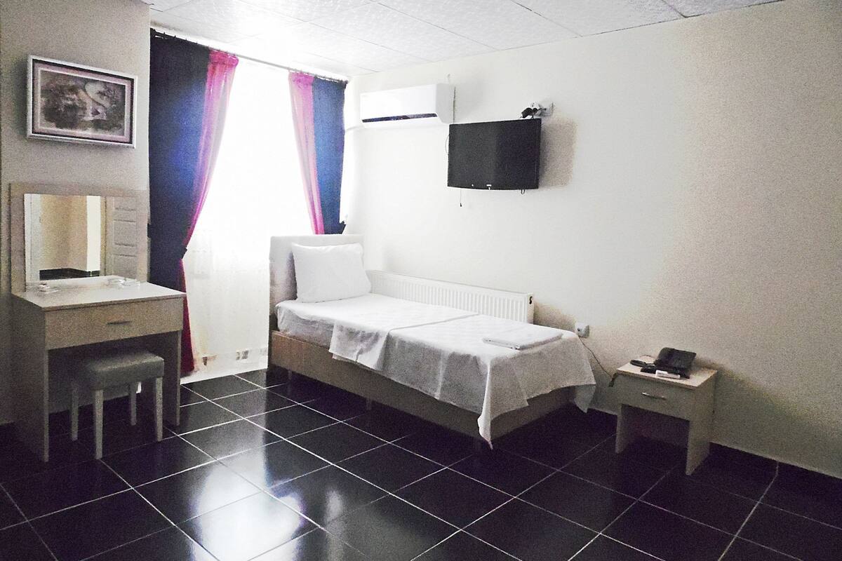 A small, clean room with a bed, a desk, a chair, a TV, and a window with curtains.