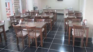 Un área de comedor con varias mesas y sillas, piso de baldosas y un televisor montado en la pared.