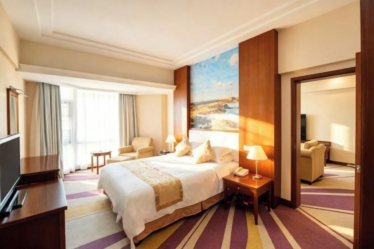 A hotel room with a large bed, a desk, a chair, a TV, and a painting on the wall.