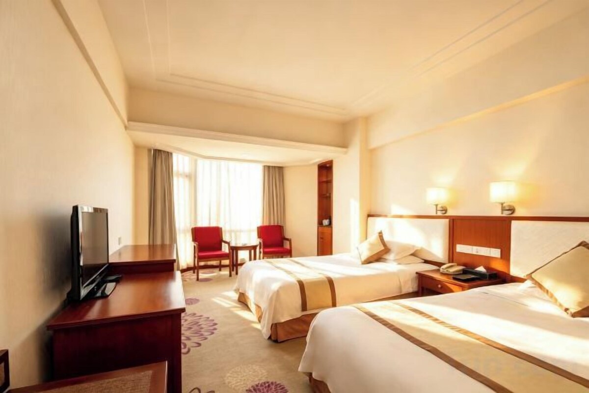 A hotel room with two beds, a desk with a TV, a chair, and a small table.