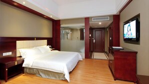 A hotel room with a large bed, a desk, a television, and a bathroom visible through a glass door. - Willman Hotel (Dongguan)