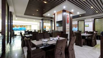 A restaurant with multiple dining tables and chairs, a modern ceiling design, and a large screen on the wall.